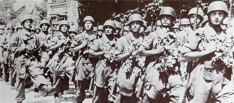 Gruppe von Soldaten in Uniform mit Helmen marschiert in einer Reihe auf einer Straße
