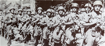 Gruppe von Soldaten in Uniform mit Helmen marschiert in einer Reihe auf einer Straße