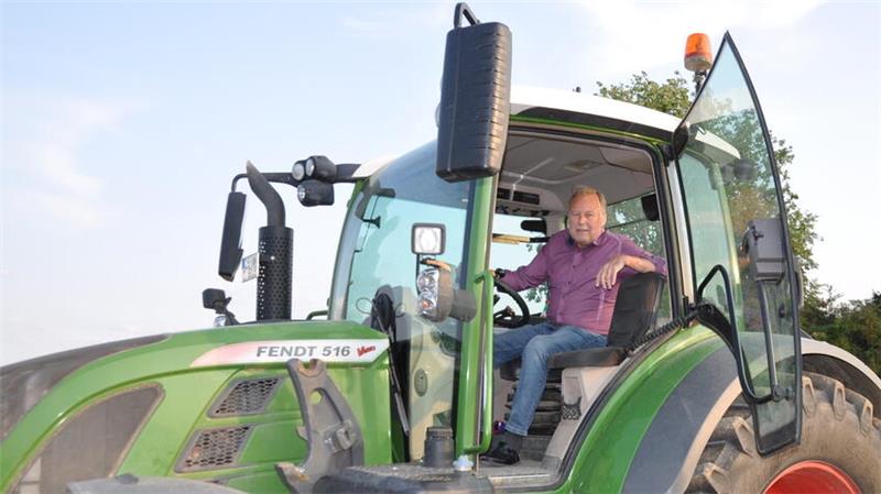 Ein Mann sitzt in der Fahrerkabine eines grünen Traktors vom Modell Fendt 516 mit geöffneter Tür.