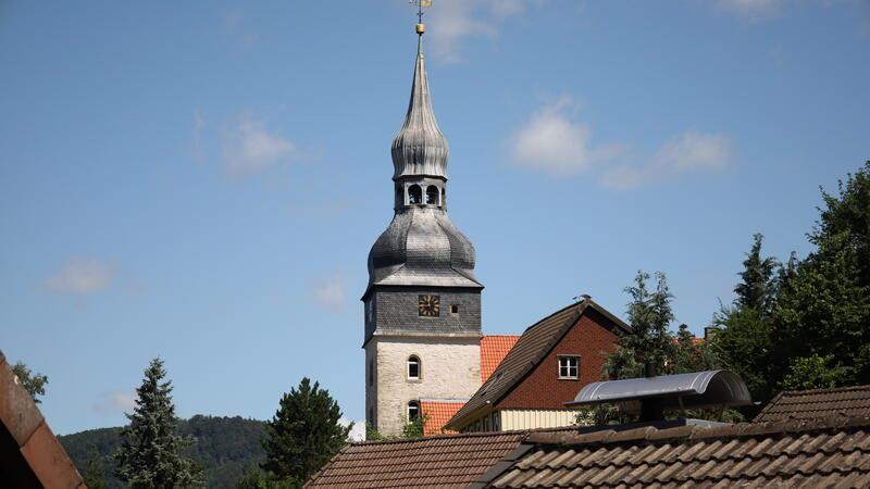 Kirchturm mit barocker Haube hinter Häuserdächern und Bäumen vor blauem Himmel