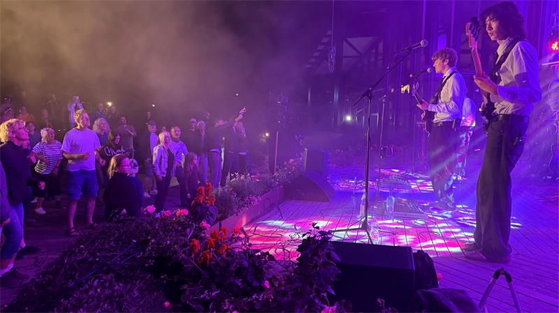 Das Foto zeigt eine Musikband auf der Bühne und tanzende Menschen davor.