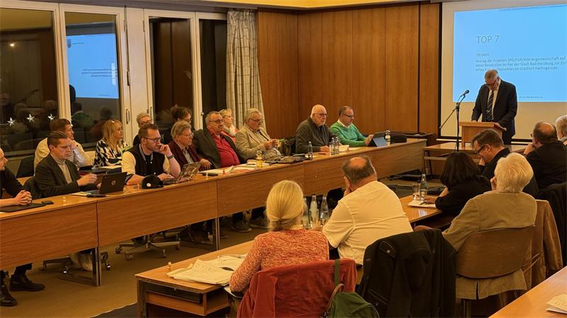 Mehrere Menschen sitzen in einem Saal an langen Tischen. Ein Stadtrat.