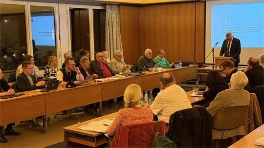 Mehrere Menschen sitzen in einem Saal an langen Tischen. Ein Stadtrat.