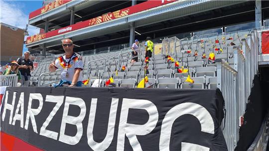 Ein Mann steht in einem leeren Stadion hinter einer Fahne mit dem Schriftzug HARZBURG.