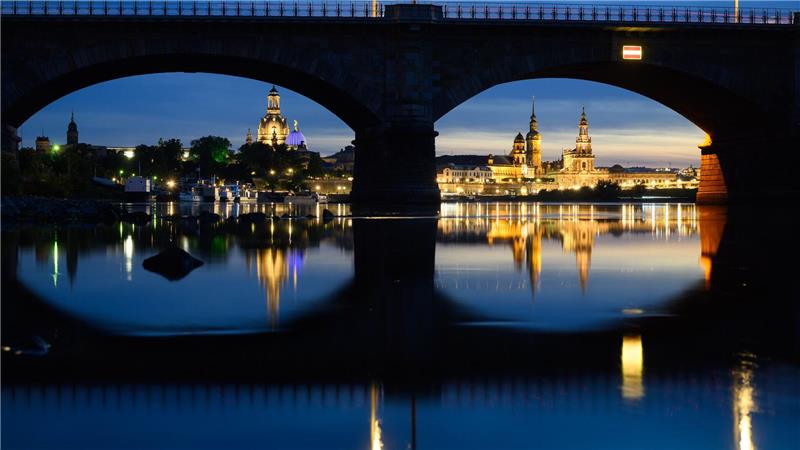 Blick am Abend in Dresden durch die Brückenbögen der Albertbrücke auf die historische Altstadtkulisse an der Elbe mit der Frauenkirche (l-r), der Kuppel der Kunstakedmie mit dem Engel „Fama“, dem Terrassenufer, dem Ständehaus, dem Hausmannsturm, der Hofkirche und der Semperoper.