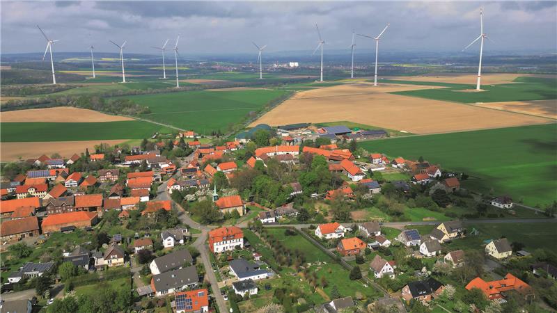 Blick auf den Bürgerwindpark: Im Vordergrund ist Beuchte zu erkennen mit der Dorfkirche und der Biogasanlage, am Horizont leuchten die Silos der Zuckerfabrik Schladen.