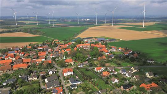 Blick auf den Bürgerwindpark: Im Vordergrund ist Beuchte zu erkennen mit der Dorfkirche und der Biogasanlage, am Horizont leuchten die Silos der Zuckerfabrik Schladen.