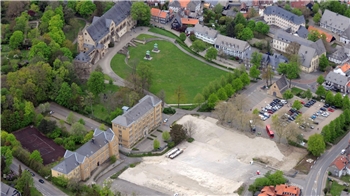 Luftaufnahme eines Parks mit mehreren historischen Gebäuden, einem großen Rasenplatz, Bäumen und einem angrenzenden Parkplatz