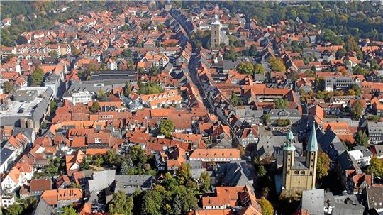 Luftaufnahme einer Stadt mit roten Dächern, mehreren Kirchtürmen und viel Grün