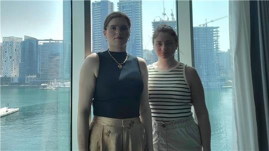 Zwei Frauen stehen in einem Hotelzimmer in Dubai, im Hintergrund sind Hochhäuser zu sehen.