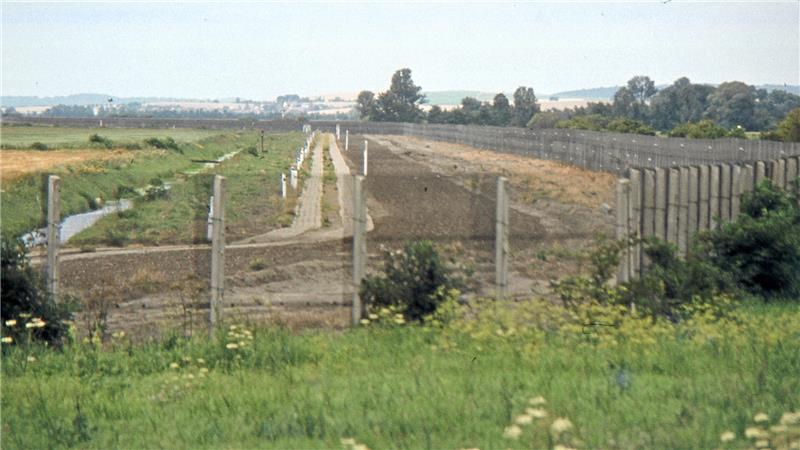 DDR-Grenzanlagen mit einem hohen Zaun ziehen sich durch eine Landschaft.