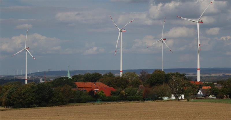 Ein Dorf mit Windenergieanlagen im Hintergrund.