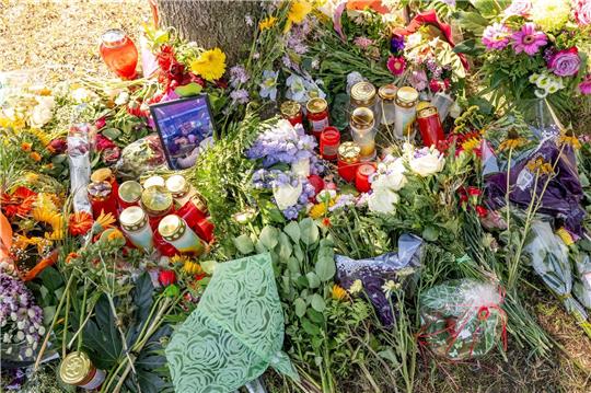 Blumen, Kerzen und Bilder liegen an einem Baum, in dessen Nähe am 17. August 2022 die tote Frau in einem Auto entdeckt wurde.