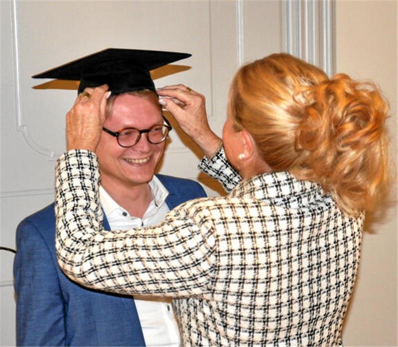 Herr des Goslarer Geldes: Dr. Pascal Bothe (CDU) mag Zahlenarbeit Frau mit hochgestecktem Haar und kariertem Blazer setzt einem jungen Mann in blauem Sakko einen schwarzen Doktorhut auf.