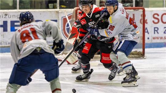 Eishockeyspieler in schwarzer und weißer Ausrüstung kämpfen um den Puck auf dem Eis vor der Bande mit Zuschauern im Hintergrund.