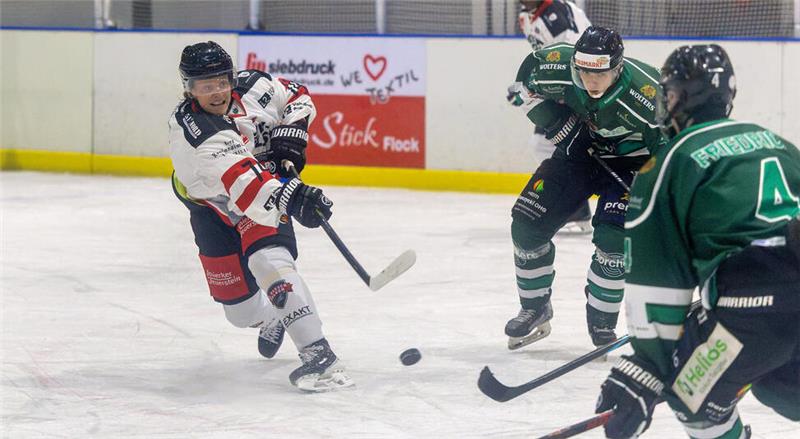 Eishockeyspieler in weiß-roter und grün-schwarzer Ausrüstung kämpfen um den Puck auf dem Eis.