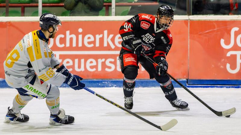 Zwei Eishockeyspieler in Aktion auf dem Eis, einer in schwarzer und roter Ausrüstung, der andere in weißer und gelber Ausrüstung