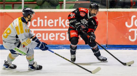 Zwei Eishockeyspieler in Aktion auf dem Eis, einer in schwarzer und roter Ausrüstung, der andere in weißer und gelber Ausrüstung