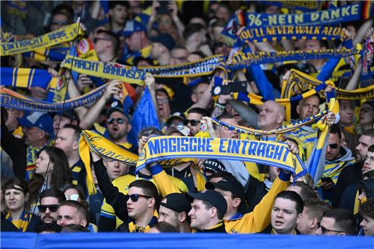 Braunschweiger Fans stehen mit ihren Schals auf der Tribüne.