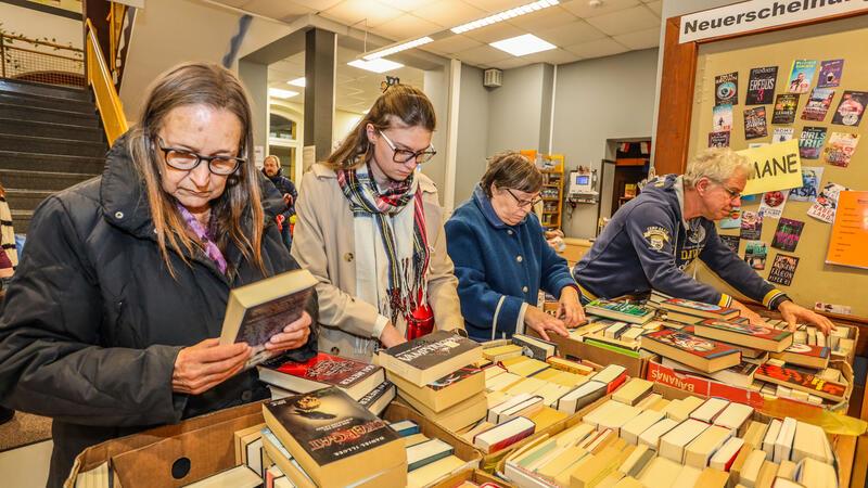 Vier Menschen stöbern in Kisten voller Bücher. Die Frau ganz links hält ein Buch in beiden Händen.