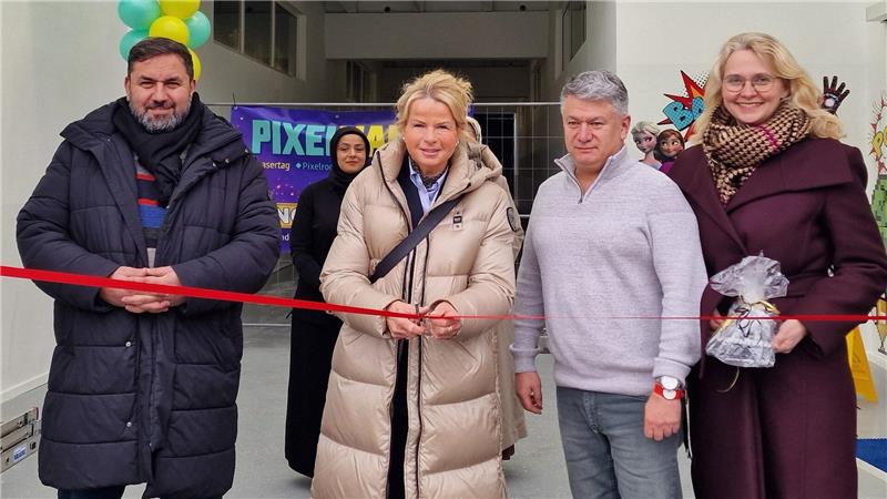 Vier Personen stehen in einem Raum mit Luftballons und halten ein rotes Band für eine Eröffnungszeremonie.