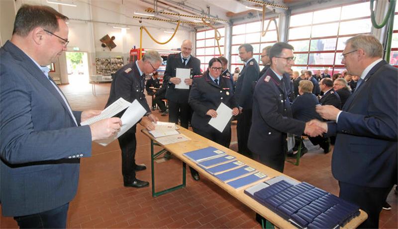 Bürgermeister Ingo Henze, Stadtbrandmeister Matthias Brunke (v.l.) und Ulrich Eberhardt, Vorsitzender des Feuerwehrausschusses (r.), verteilen die Urkunden und Ehrennadeln an die Einsatzkräfte.