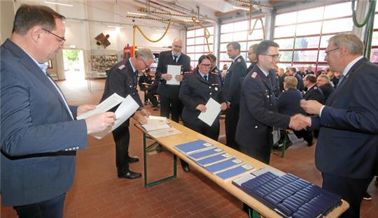 Bürgermeister Ingo Henze, Stadtbrandmeister Matthias Brunke (v.l.) und Ulrich Eberhardt, Vorsitzender des Feuerwehrausschusses (r.), verteilen die Urkunden und Ehrennadeln an die Einsatzkräfte.