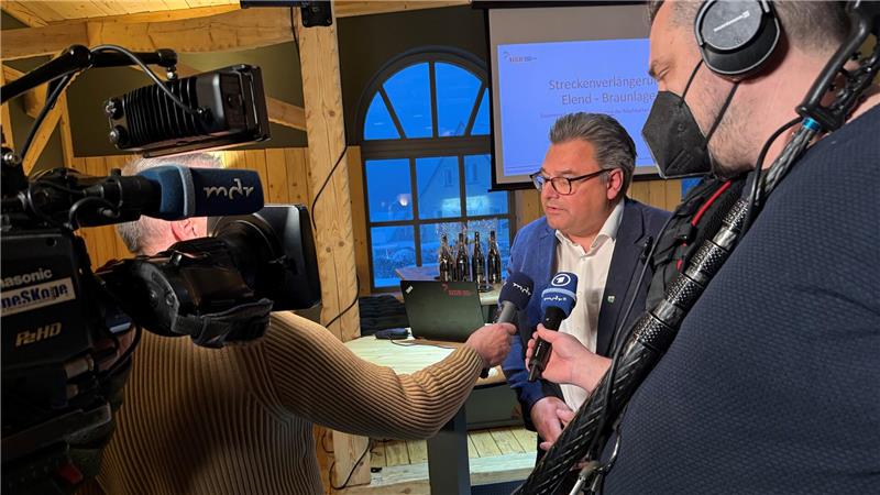 Ein Mann spricht vor einer Fernsehkamera in zwei Mikrofone.