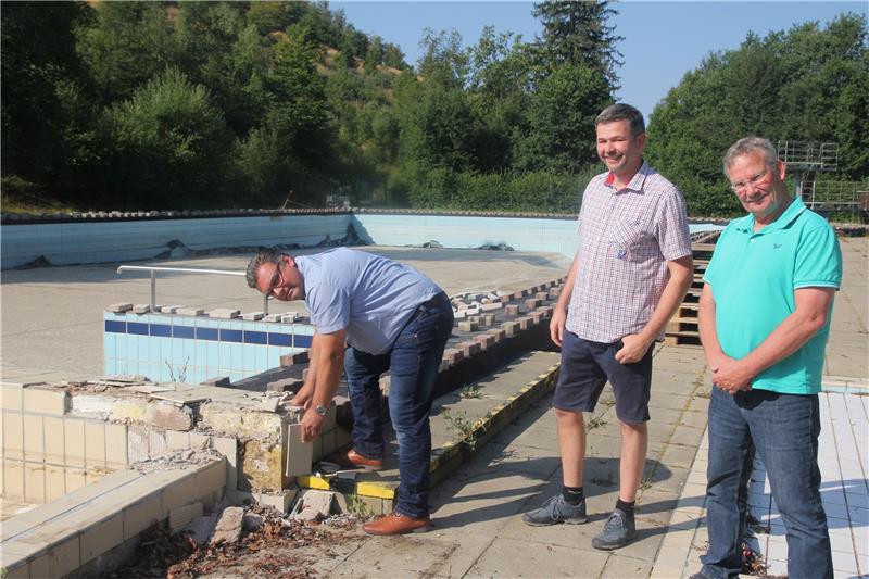 Im Freibad Hohegeiß starten die Arbeiten – inoffiziell Bürgermeister Wolfgang Langer (links) zeigt, wie porös der obere Teil der Schwimmerbecken-Umrandung ist: Mit der bloßen Hand holt er im Beisein von Ortsvorsteher Sebastian Hansmann und Bauamtsleiter Thomas Reiß (rechts) Fliesen herunter.  Foto: Eggers