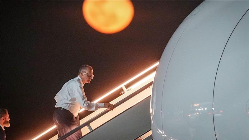 Bundeskanzler Friedrich Merz geht die Gangway vor dem aufgehenden Mond hinauf.