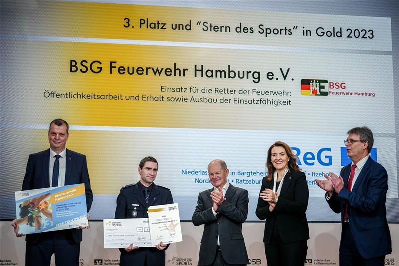 Ehrenamt: Zwei Vereine aus dem Norden ausgezeichnet Bundeskanzler Olaf Scholz (SPD, M) zeichnet zusammen mit Thomas Weikert (r), Präsident des Deutschen Olympischen Sportbundes (DOSB), und Marija Kolak (2.v.r), Präsidentin des Bundesverbandes der Deutschen Volksbanken und Raiffeisenbanken (BVR), bei der Verleihung der «Sterne des Sports» in Gold die BSG Feuerwehr Hamburg mit dem 3. Platz aus.