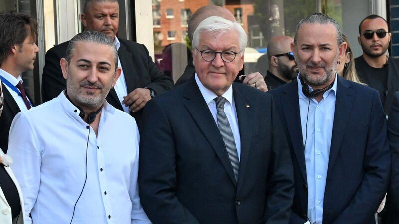 Bundespräsident Frank-Walter Steinmeier (M) zusammen mit Hasan Yildirim (l) und Özcan Yildirim vor ihrem Friseurgeschäft. Am 9. Juni 2024 hatten die NSU-Terroristen Mundlos und Böhnhardt in der Kölner Keupstraße vor dem Friseurgeschäft eine Nagelbombe gezündet.