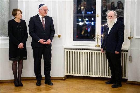 Bundespräsident Frank-Walter Steinmeier und seine Frau Elke Büdenbender sowie Yehuda Mansbach (r), der Enkel von Rabbiner Arthur Posner, bei der gemeinsamen Chanukka-Feier im Schloss Bellevue. Auf der Fensterbank steht der Chanukka-Leuchter der Familie Posner.
