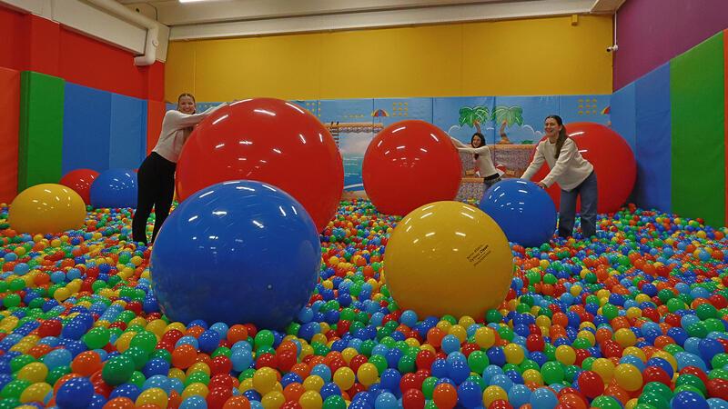 Drei Frauen in einem Raum mit buntem Bällebad und mehreren großen bunten Bällen