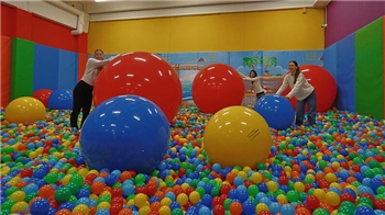 Drei Frauen in einem Raum mit buntem Bällebad und mehreren großen bunten Bällen