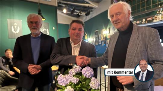 Das Bild zeigt drei Männer, von denen einer denjenigen beglückwünscht, der Blumen in der Hand hält.