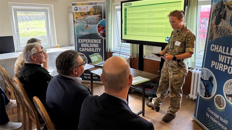 Das Foto zeigt eine Frau in Uniform, die vor vielen sitzenden Menschen steht und spricht.