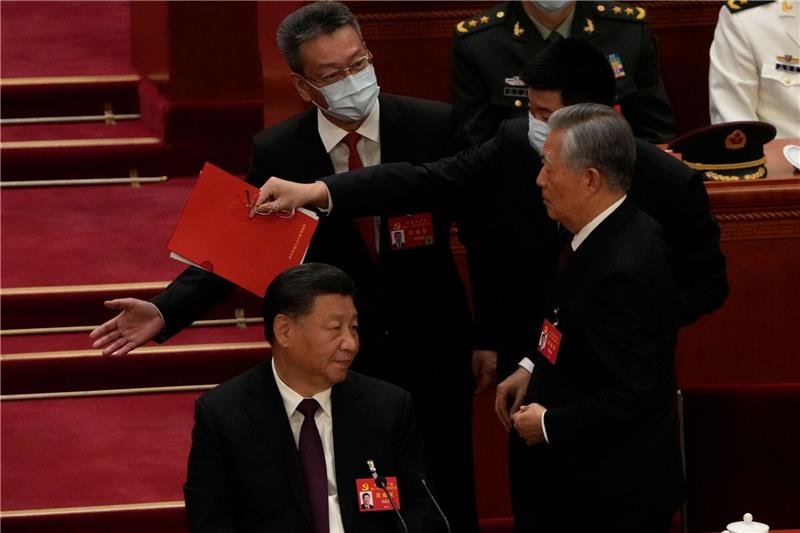 Dritte Amtszeit: Xi Jinping baut seine Macht weiter aus Chinas Ex-Präsident Hu Jintao (r) wird von seinem Platz weg begleitet. Links sitzt Xi Jinping und guckt zu.
