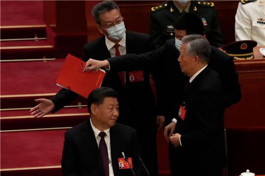 Chinas Ex-Präsident Hu Jintao (r) wird von seinem Platz weg begleitet. Links sitzt Xi Jinping und guckt zu.