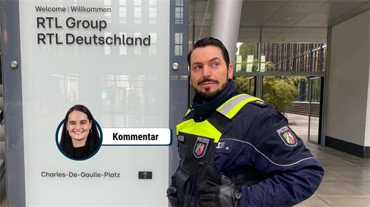 Polizist in dunkler Uniform mit reflektierenden Streifen steht vor einem Schild mit der Aufschrift 'RTL Group RTL Deutschland'.