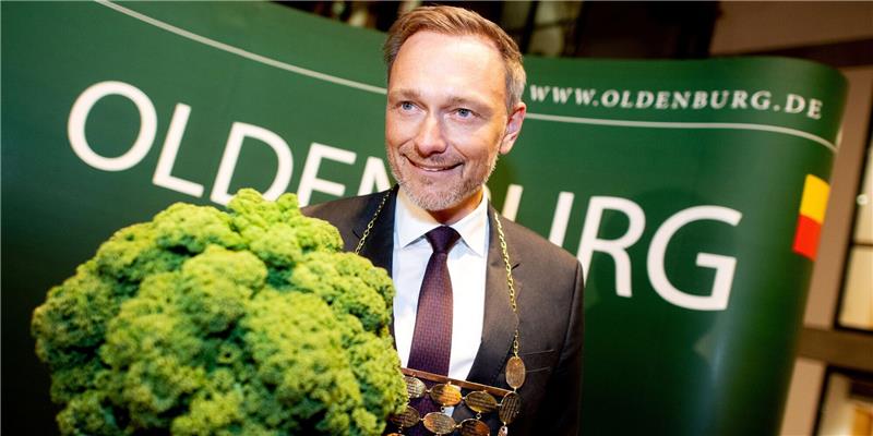 Christian Lindner (FDP), Bundesfinanzminister, trägt eine Kohlkette und hält eine Grünkohlpflanze, auch bekannt als „Oldenburger Palme“, in den Händen.