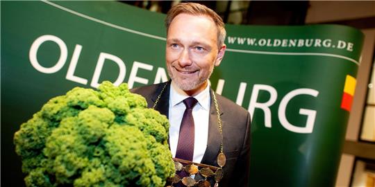 Christian Lindner (FDP), Bundesfinanzminister, trägt eine Kohlkette und hält eine Grünkohlpflanze, auch bekannt als „Oldenburger Palme“, in den Händen.