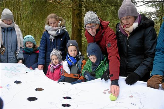 Christine Ludwig, zertifizierte Waldpädagogin, gleicht das Fehlen von Schnee mit einer Fülle von Ideen aus: Hier packt sie eine alte Damasttischdecke aus, die einen Waldparcours darstellt: Das „Reh“ (der Ball) muss mit vereinten Kräften aller, die das Tuch in Waage halten, den Gefahren (Löchern) trotzen und den Weg zurück in den Wald finden. Fotos: Kempfer