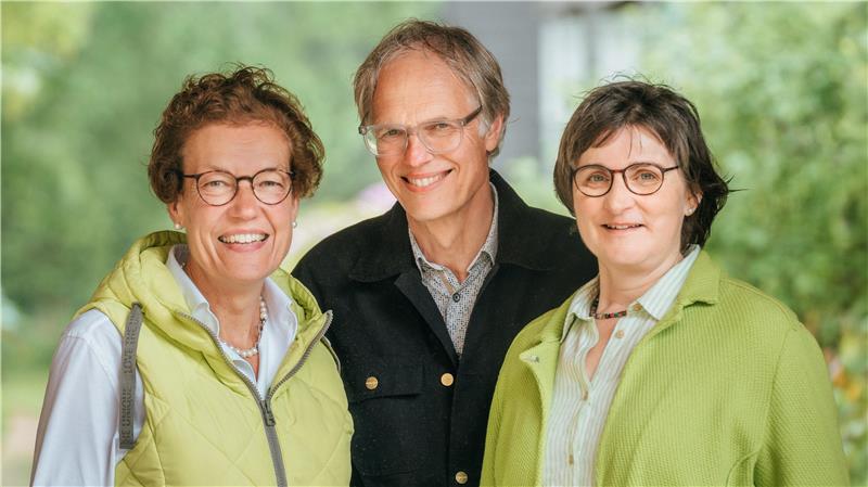 Das Foto zeigt einen Mann und zwei Frauen, die freundlich in die Kamera blicken.