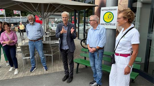 Das Foto zeigt Menschen vor einer grünen Bank.