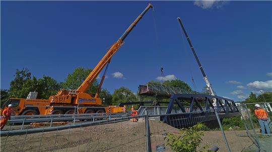 Da legt sie sich nieder: Zwei 180-Tonnen-Kräne platzieren die Behelfsbrücke zum Auseinanderbauen auf die neue Okerbrücke.