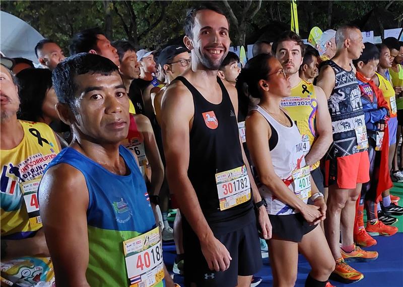 Mehrere Läufer in Sportkleidung stehen an der Startlinie eines nächtlichen Laufs auf farbigen Matten.