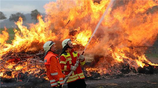 Damit das Osterfeuer nicht auf angrenzende Bäume überspringt, benetzen in Nauen die Einsatzkräfte der Feuerwehr die Vegetation mit Wasser.