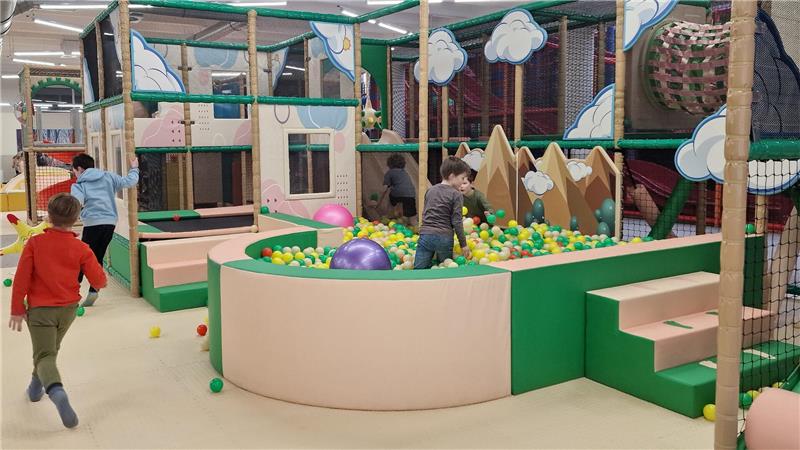 Kinder spielen in einem Indoor-Spielplatz mit Bällebad, Klettergerüsten und weichen Spielmodulen.