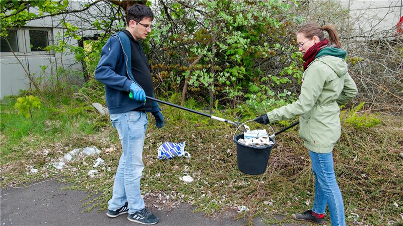 TU Clausthal und Bergschule feiern 250. Geburtstag Das Foto zeigt einen Studenten und eine Studentin, die mit Eimer und Greifarmen Müll auf dem Campus aufsammeln.